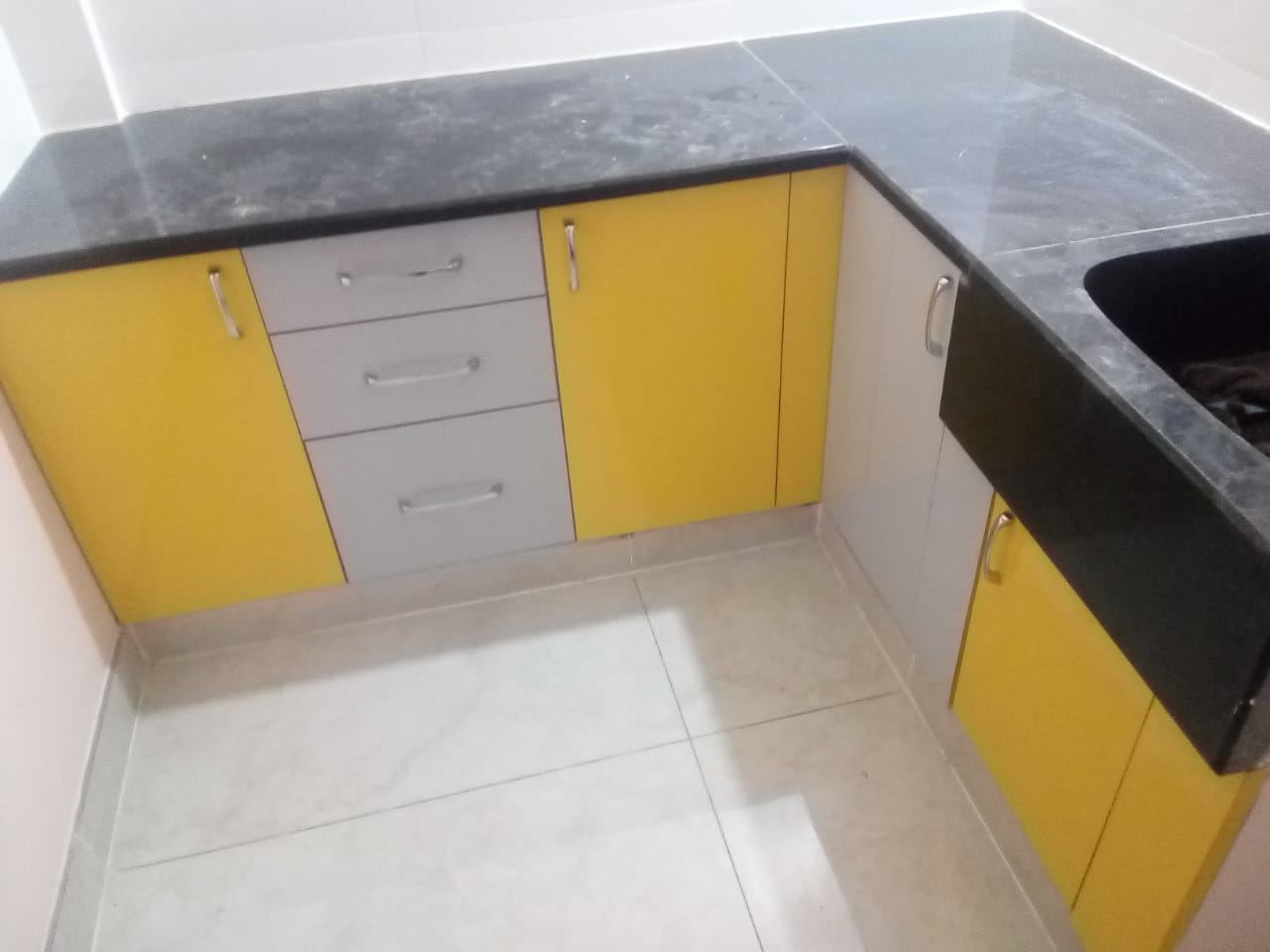 Yellow and grey kitchen base units with a black granite counter and sink